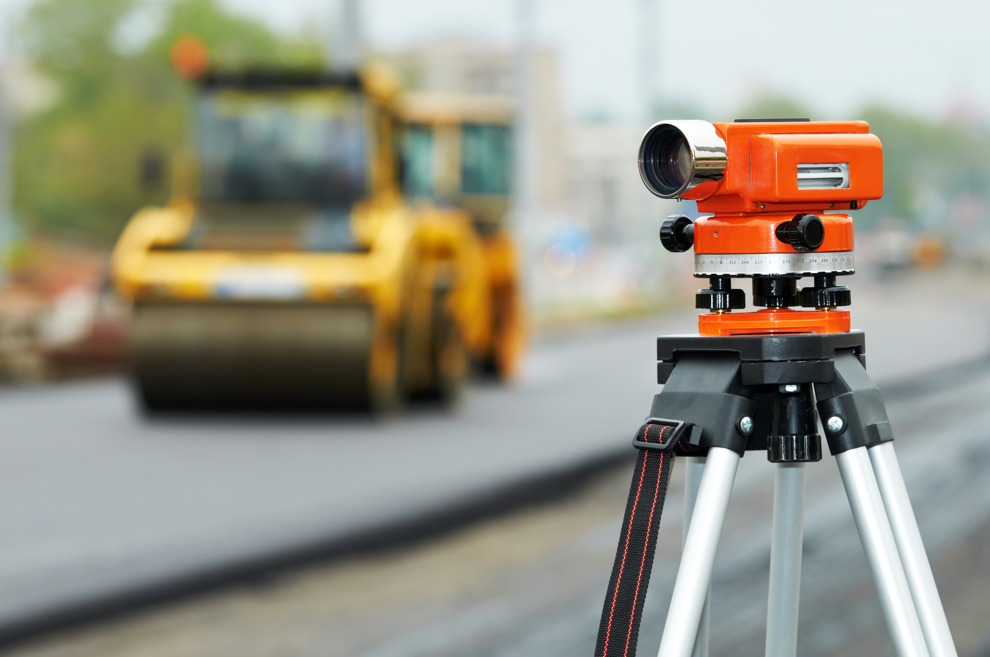 Construction surveyor equipment theodolite level tool during asphalt paving works with compactor roller at background